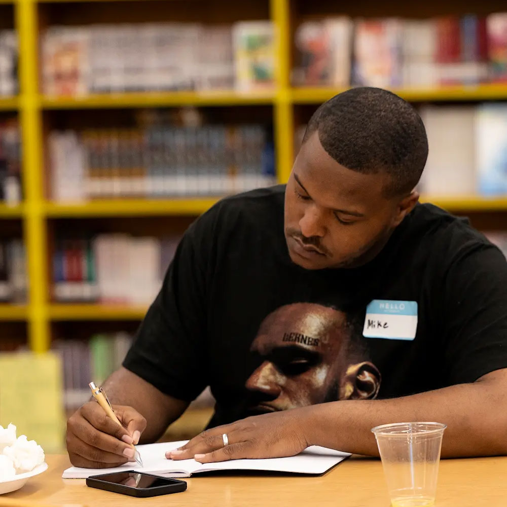 A teacher resident sitting at a table in a school's library writing on a worksheet.